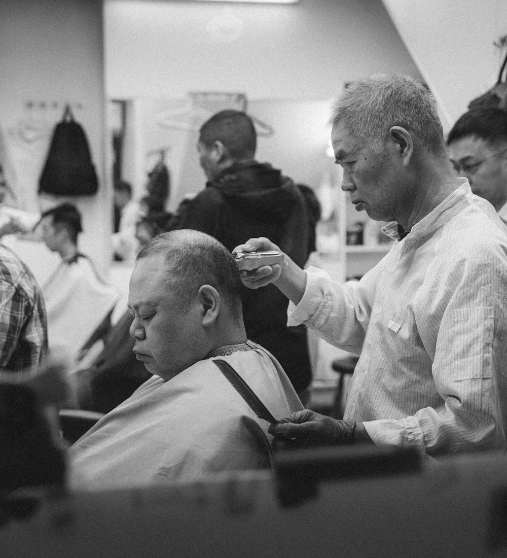 Barbeiro cuidando do cabelo de um cliente em uma barbearia movimentada